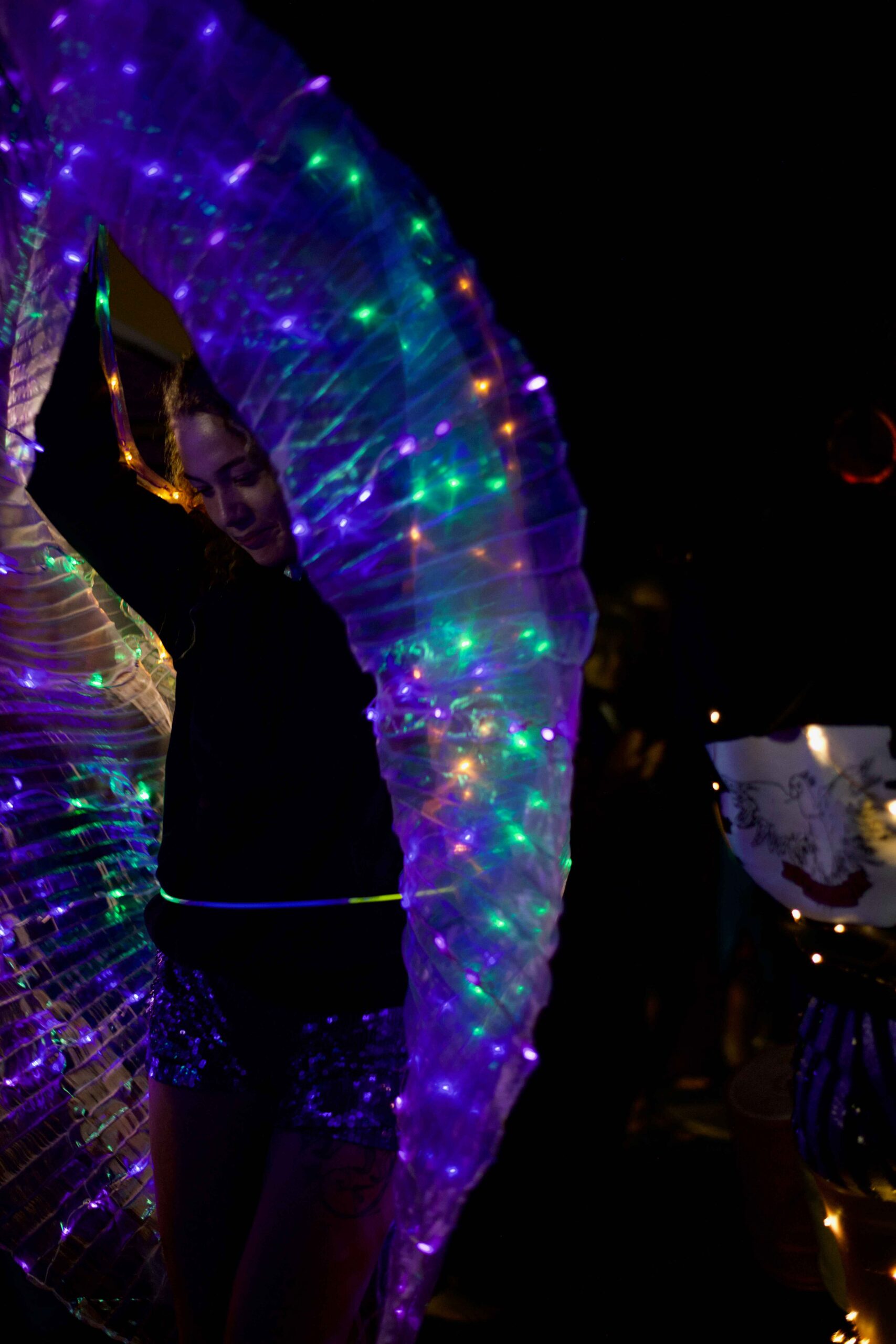 Concrete Club A person in dark clothing is under a swirl of colorful, illuminated fabric, creating a vibrant light display in a dark setting.